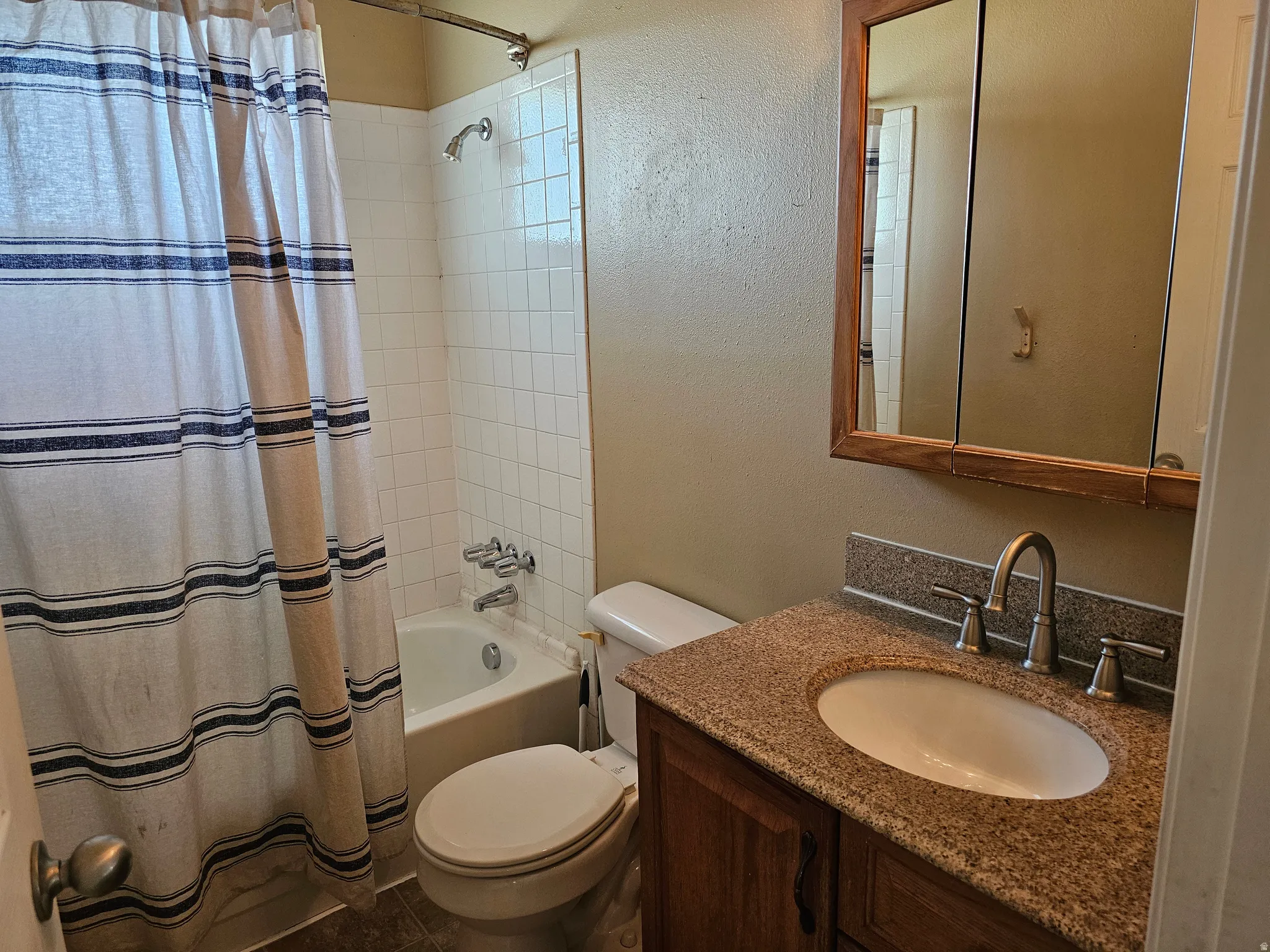Bathroom featuring a vanity with a stone-look countertop, an undermount sink, a chrome-finish faucet, and a framed medicine cabinet
