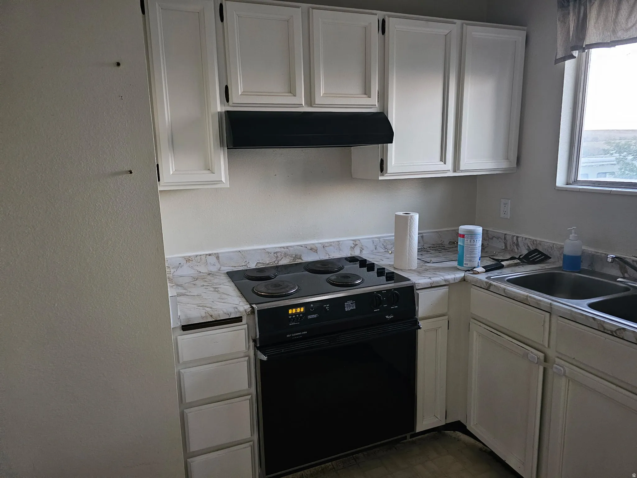 Kitchen featuring white cabinetry, black range with oven, and a double basin stainless steel sink
