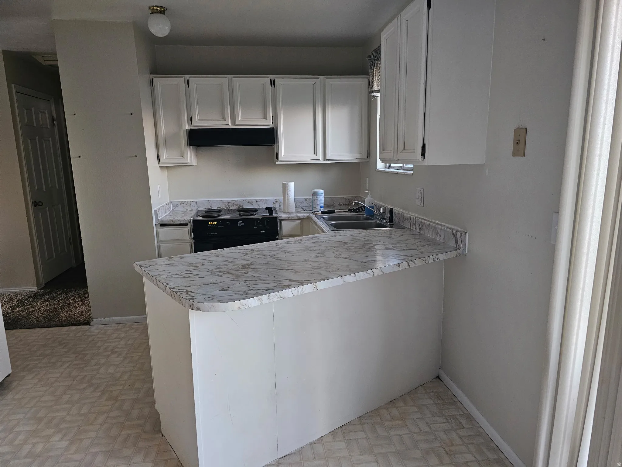 Kitchen featuring white cabinetry, a black range, a double basin sink, and a breakfast bar with a light-colored countertop