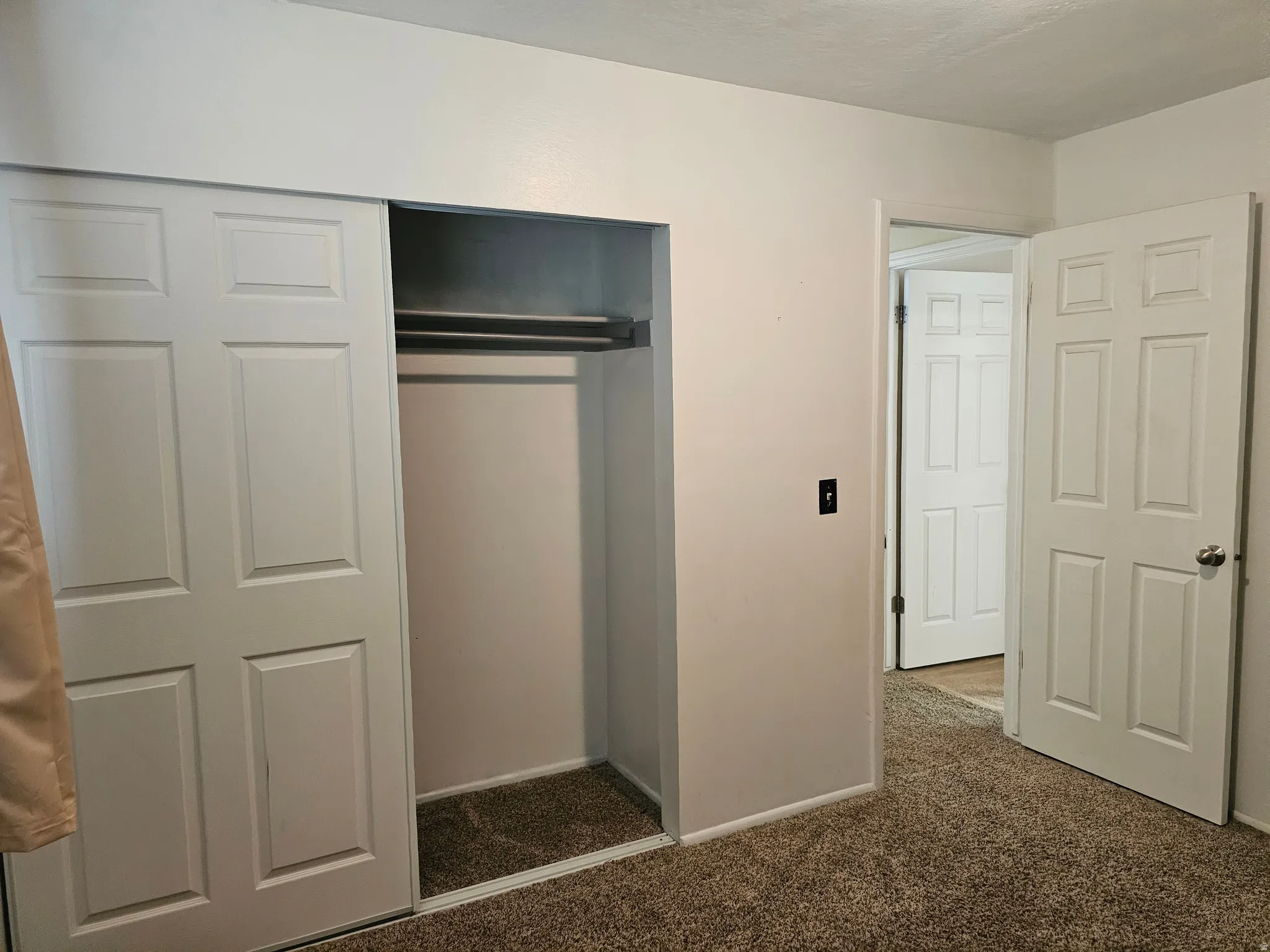 Spacious bedroom with dual closet storage featuring six-panel doors, neutral carpeting, and multiple entry points