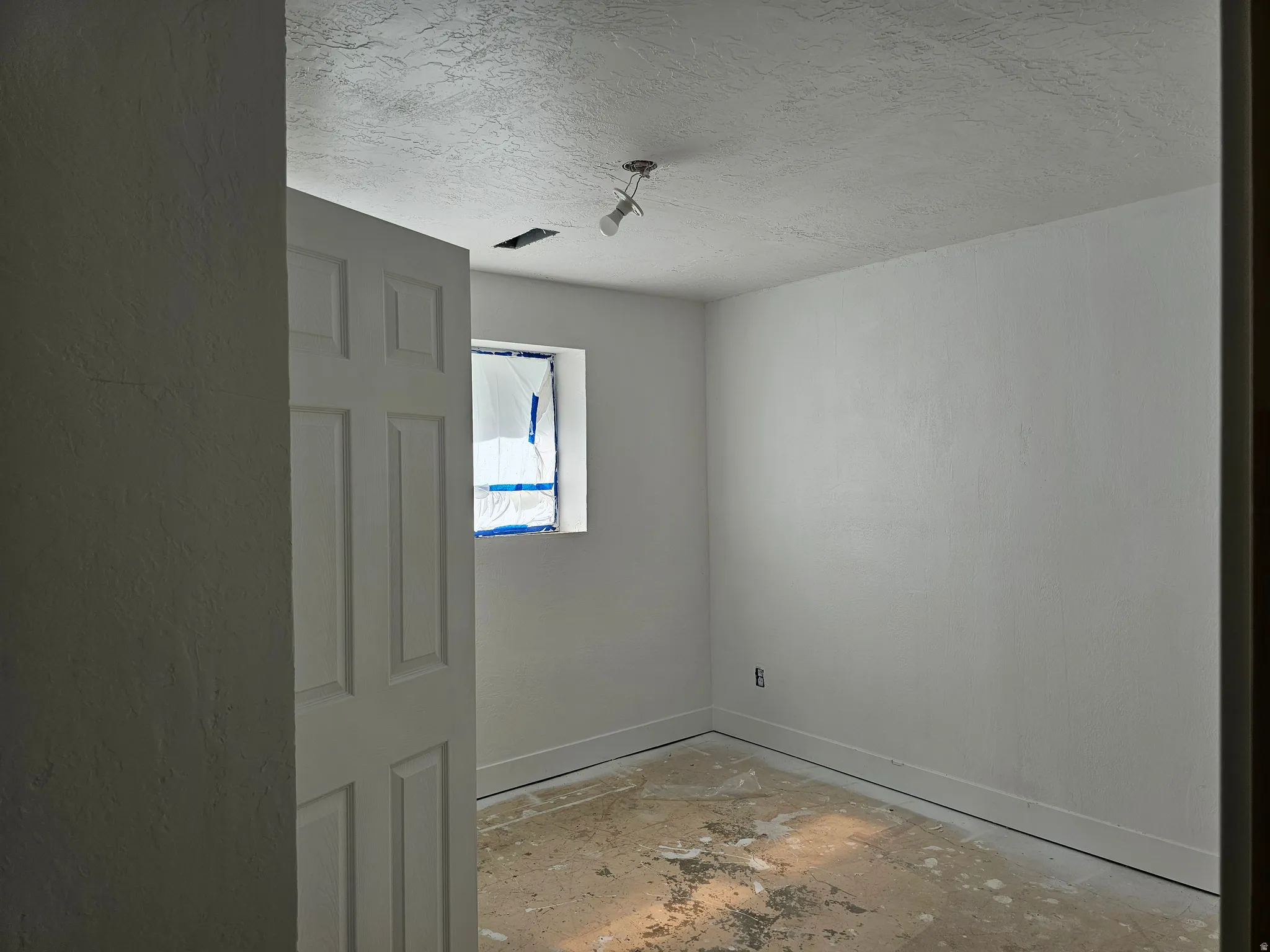 Interior room featuring a white paneled door, window opening, white walls, and a ceiling light fixture