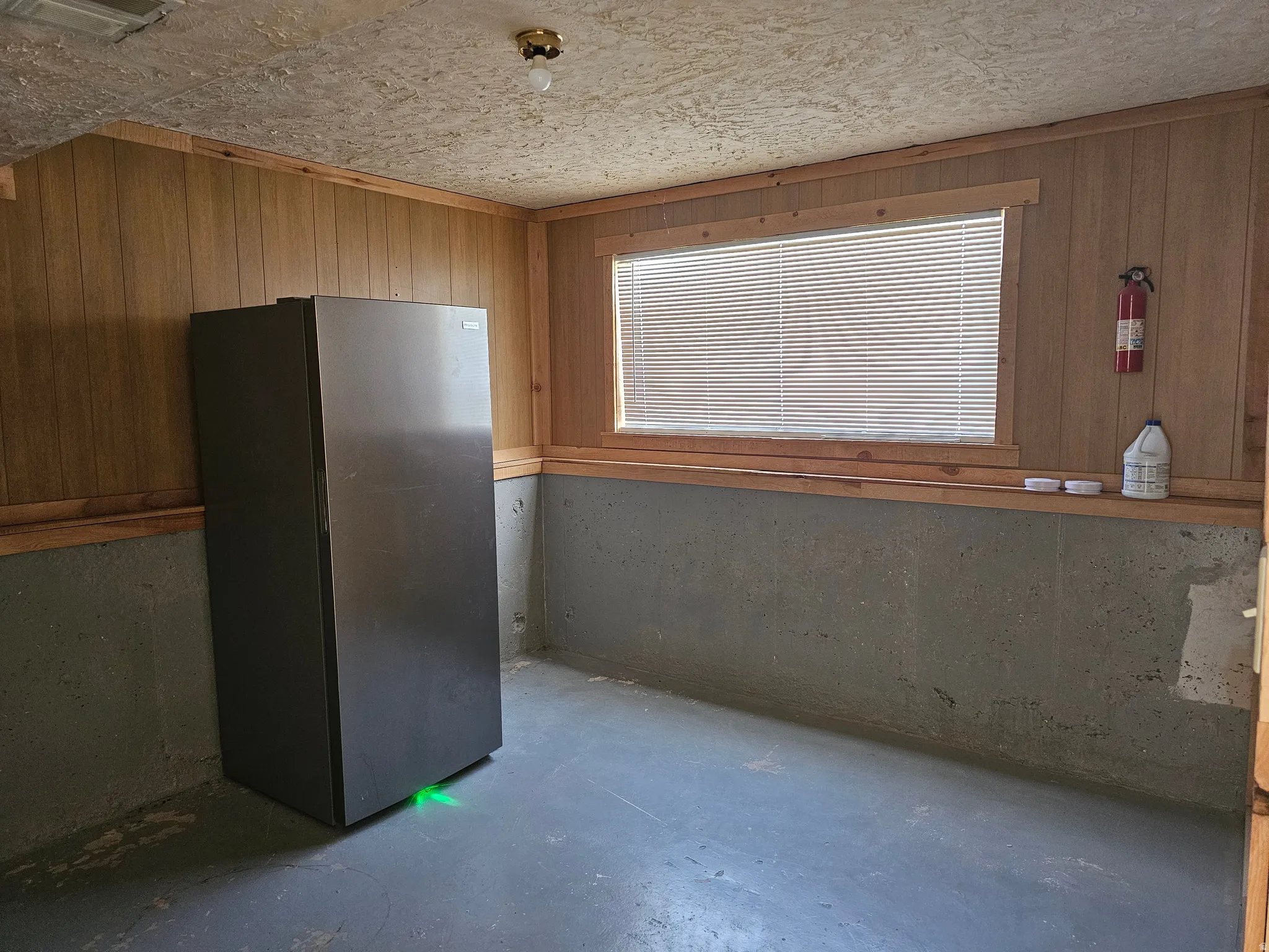 Wood-paneled walls with painted concrete flooring and a surface-mounted light fixture