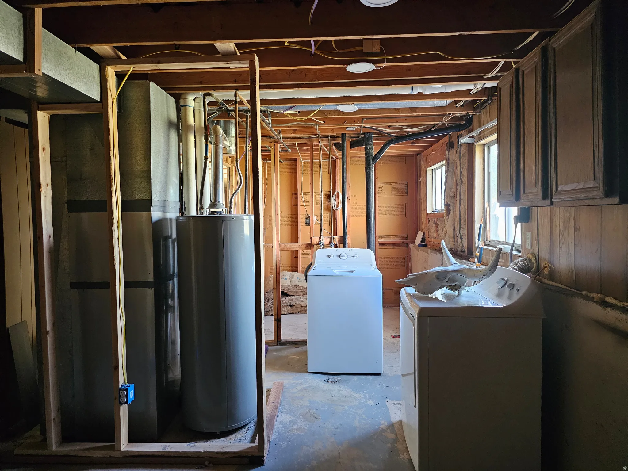Exposed ceiling joists, wood-paneled walls, multiple windows, and existing utility connections