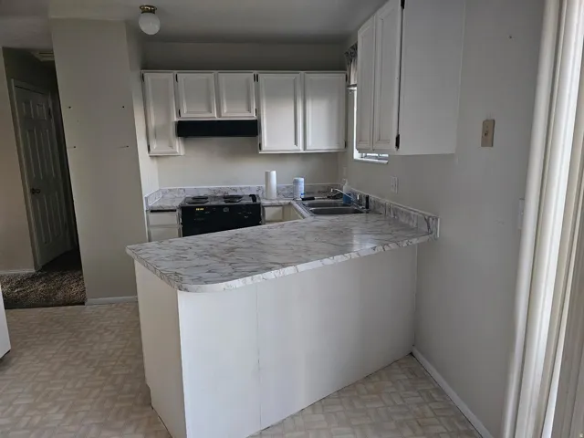 Kitchen featuring white cabinetry, a black range, a double basin sink, and a breakfast bar with a light-colored countertop