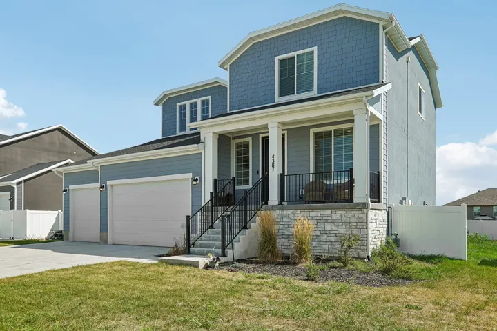 Two-story residence featuring light blue siding, a stone veneer foundation, a covered front porch, and a two-car garage
