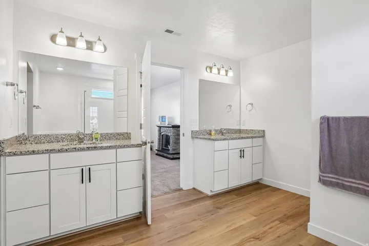 Dual vanity with white cabinetry, granite countertops, and wood-finish flooring