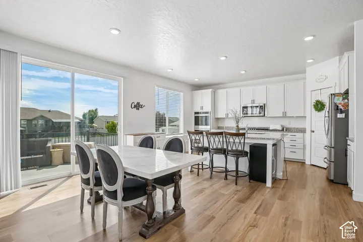 Open-concept kitchen and dining area featuring light wood-finish flooring, white cabinetry, integrated stainless steel appliances, a kitchen island with seating, and a sliding glass door to an outdoor deck