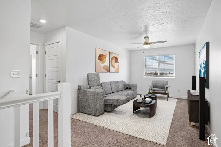 Carpeted living area featuring a ceiling fan with integrated lighting, a window with horizontal blinds, and a built-in media console
