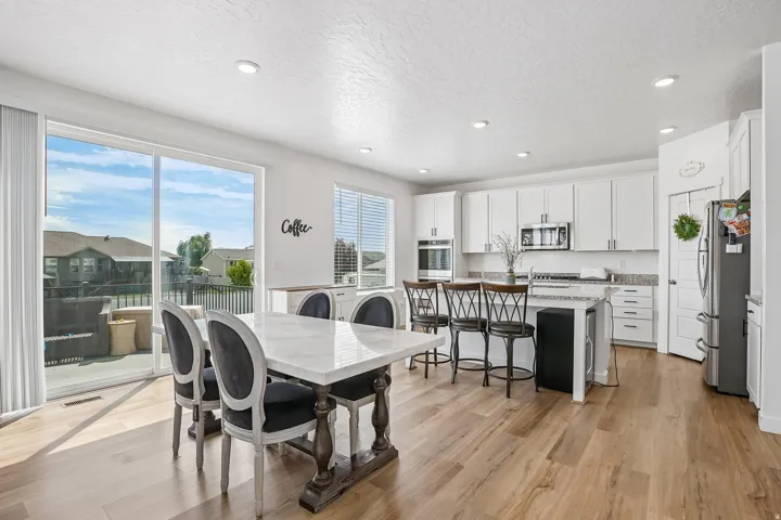 Open-concept kitchen and dining area featuring light wood-finish flooring, white cabinetry, integrated stainless steel appliances, a kitchen island with seating, and a sliding glass door to an outdoor deck