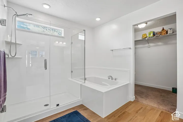 Glass-enclosed shower with a transom window, built-in soaking tub, wood-finish flooring, and recessed lighting