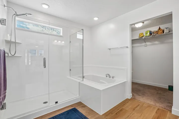 Glass-enclosed shower with a transom window, built-in soaking tub, wood-finish flooring, and recessed lighting