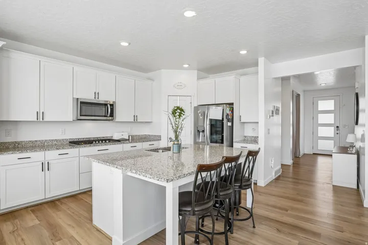 White shaker-style cabinetry, stainless steel appliances, speckled stone countertops, and wood-finish flooring