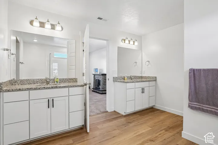 Dual vanity with white cabinetry, granite countertops, and wood-finish flooring