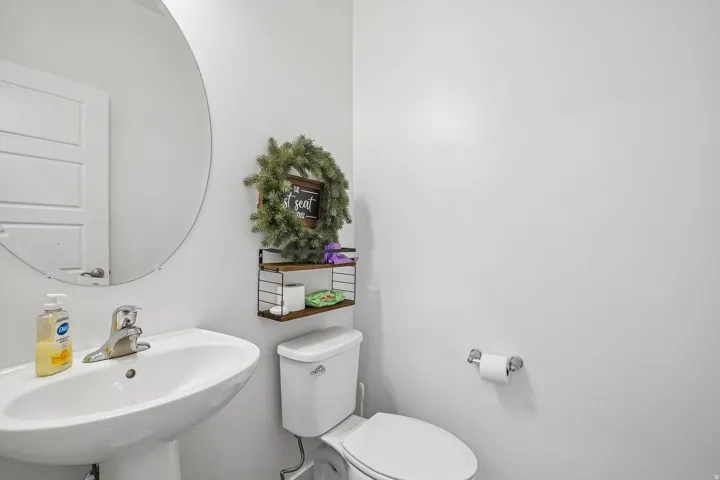 Pedestal sink with chrome faucet, circular wall mirror, and a white toilet