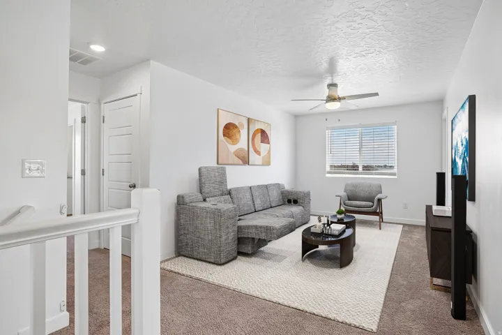 Carpeted living area featuring a ceiling fan with integrated lighting, a window with horizontal blinds, and a built-in media console