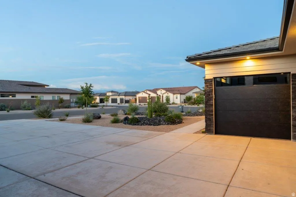 Concrete driveway with integrated walkway, modern garage door with upper window panels, stacked stone architectural accents, and desert-inspired landscaping