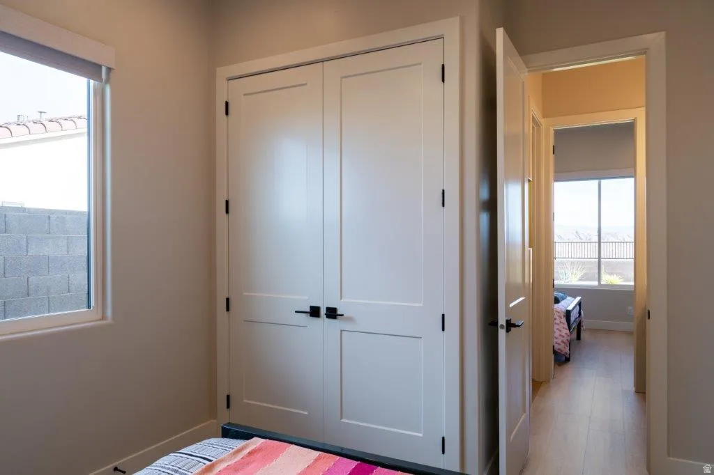 Recessed window with roller shade, neutral wall paint, double panel closet doors with matte black hardware, and wood-finish flooring