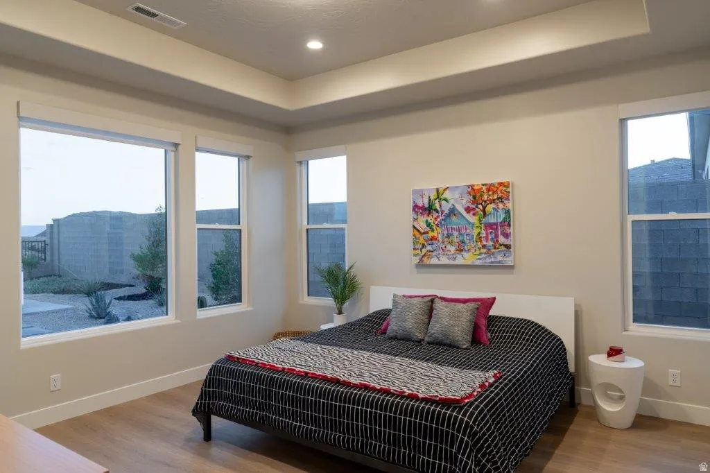 Tray ceiling with recessed lighting, multiple windows, wood-finish flooring, and light-toned walls