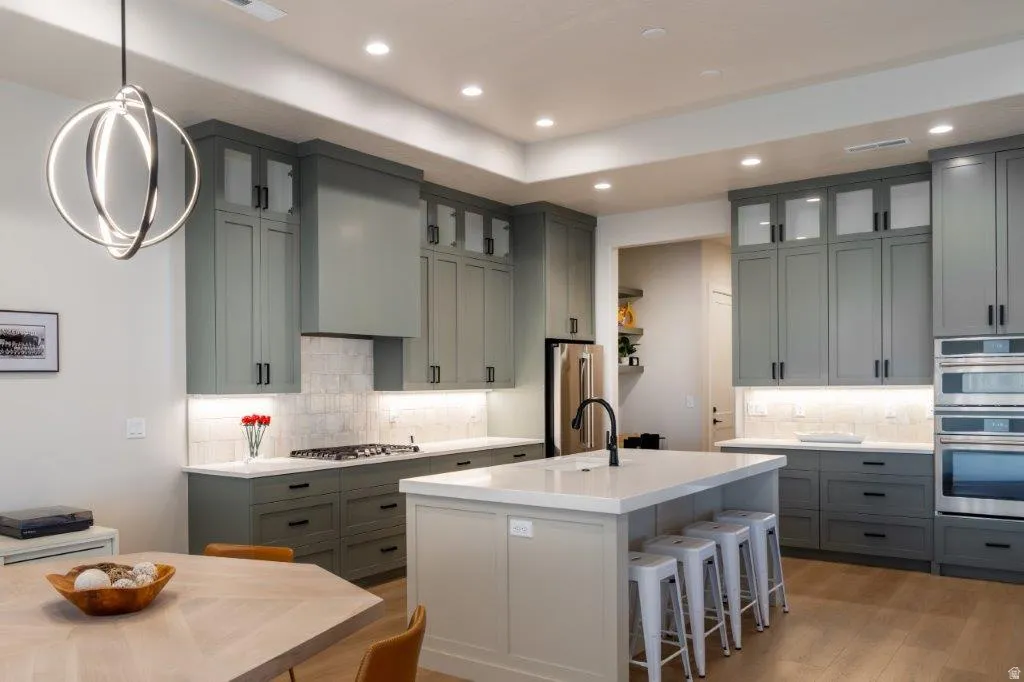 Modern kitchen featuring light green cabinetry, integrated stainless steel appliances, a central island with a solid surface countertop, and wood-finish flooring