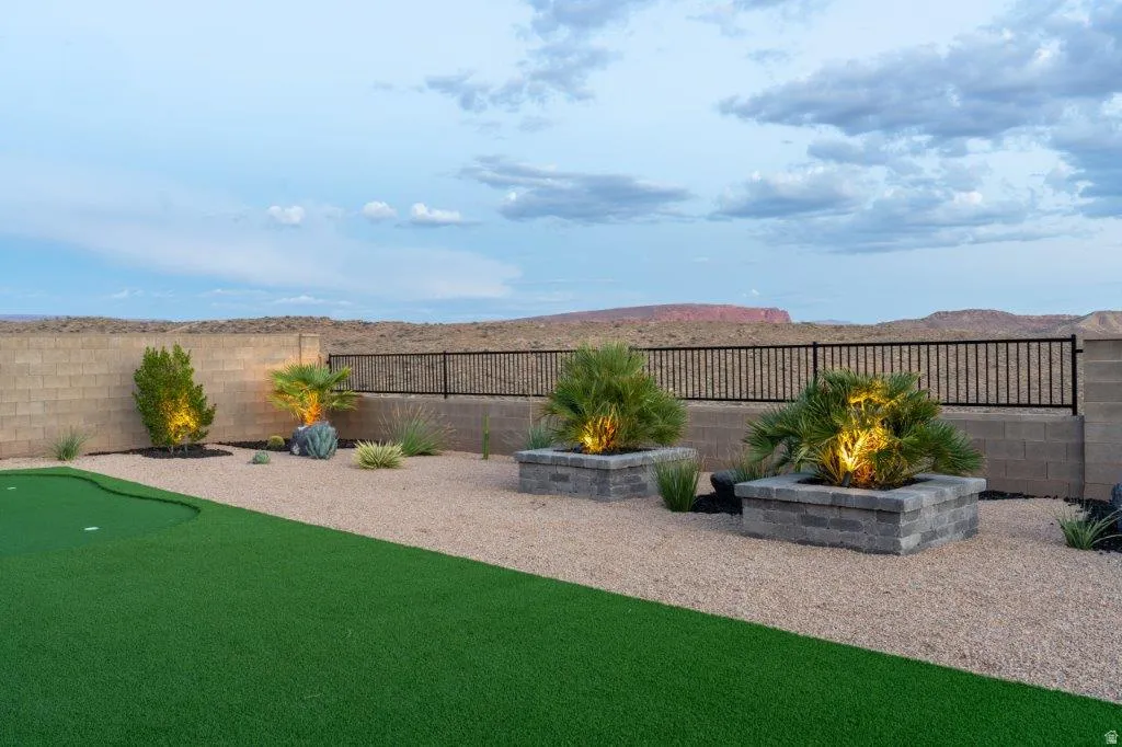 Expansive backyard oasis featuring professionally manicured synthetic turf, decorative planter beds with landscape lighting, desert-adapted plantings, and a metal-finish perimeter fence