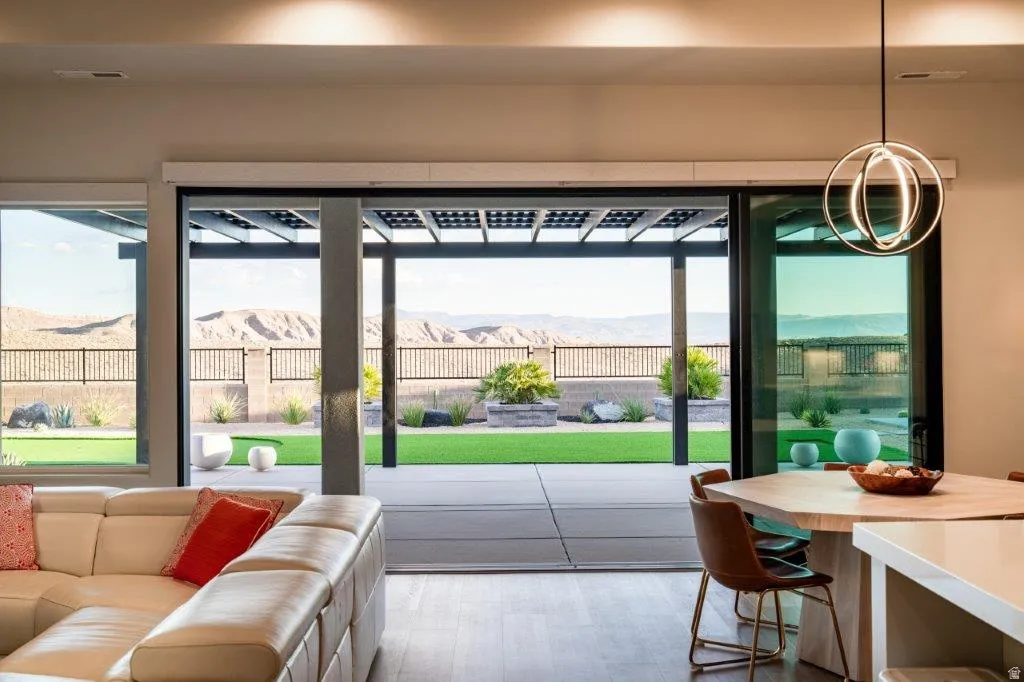 Expansive sliding glass doors, covered patio with pergola, artificial turf lawn, built-in planters, and mountain backdrop