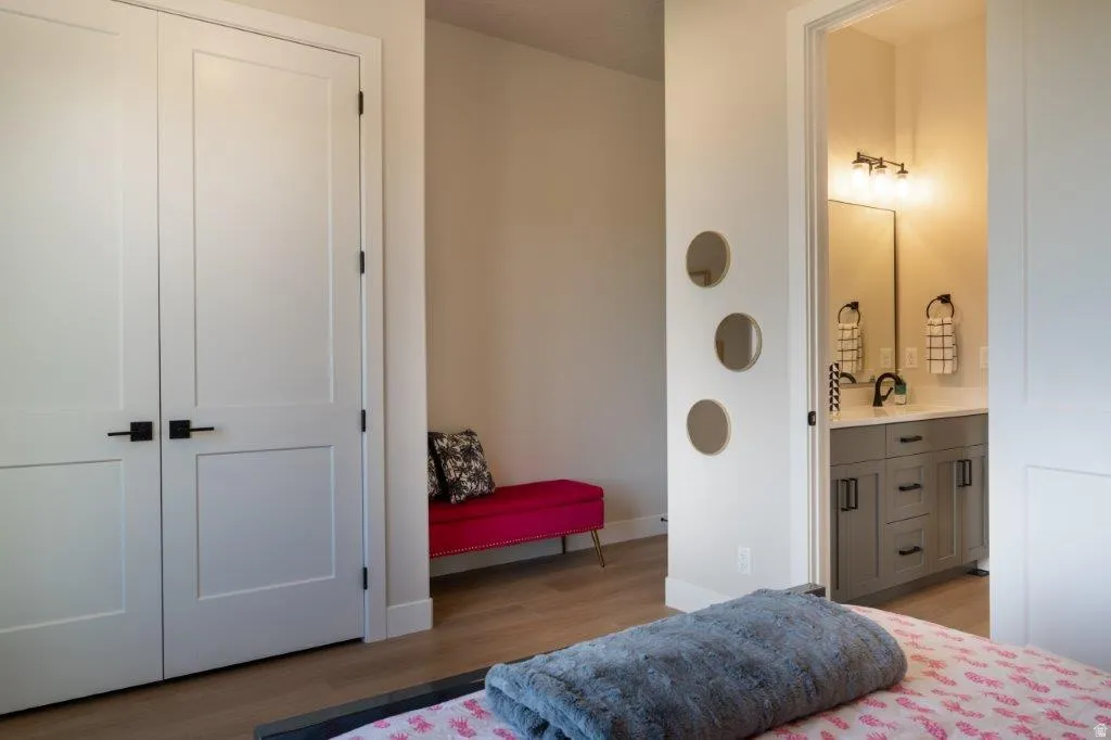Wood-finish flooring, white panel doors with matte black hardware, gray vanity with quartz countertop, black faucet, and three-light vanity fixture
