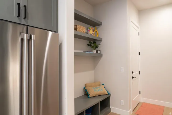 Stainless steel refrigerator, gray cabinetry with black hardware, built-in shelving, built-in bench with storage, and a white panel door with black hardware