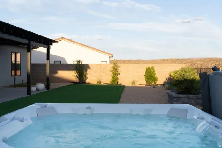 Built-in spa with water feature, artificial turf, gravel landscaping, and covered patio with dark-framed posts