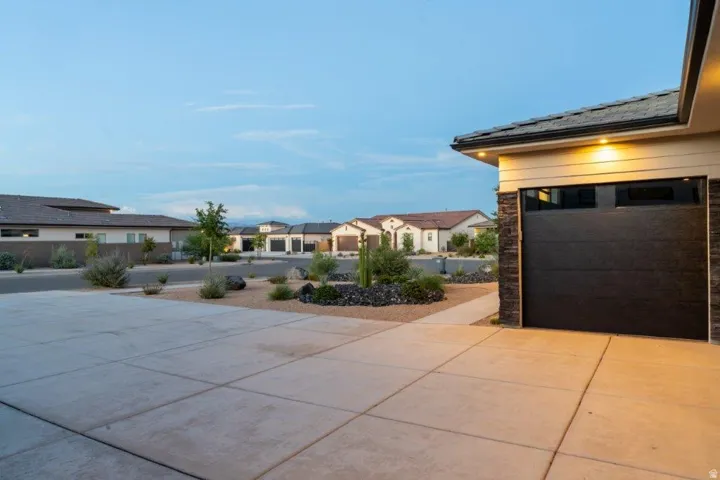 Concrete driveway with integrated walkway, modern garage door with upper window panels, stacked stone architectural accents, and desert-inspired landscaping