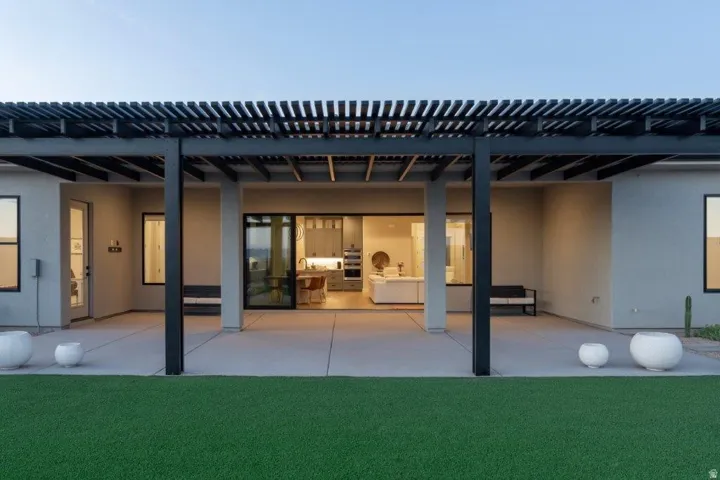 Expansive outdoor patio with a black slatted pergola, concrete flooring, and synthetic turf lawn