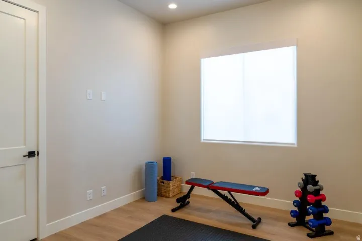 Dedicated home fitness room featuring wood-finish flooring, recessed ceiling lighting, a large bright window with natural light, and white painted walls