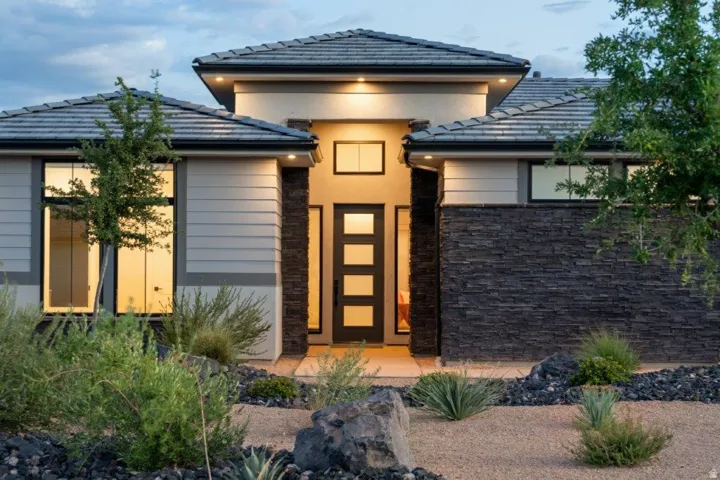 Modern architectural home showcasing a striking facade with warm-toned stucco exterior, black tile roofing, and a central entry tower featuring horizontal wood-grain doors and sidelights