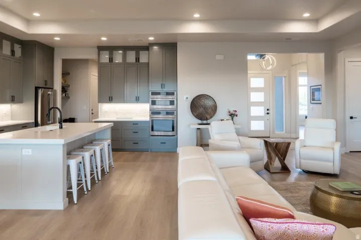 Open-concept living area with wood-finish flooring, a contemporary kitchen featuring integrated stainless steel appliances, a kitchen island with seating, recessed lighting, and a modern entry door with decorative glass panels