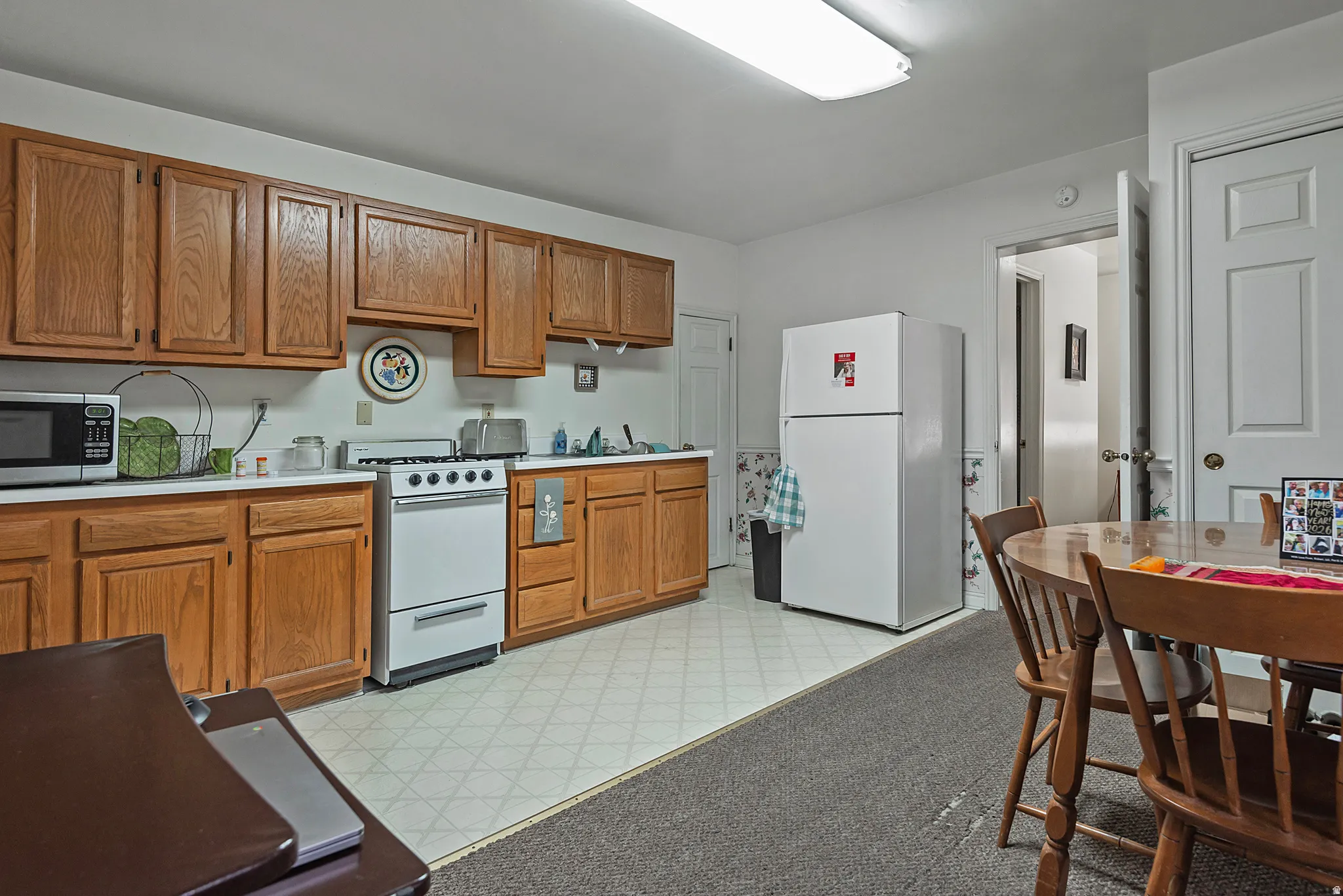 Kitchen with wood-finish cabinetry, white countertops, and white appliances