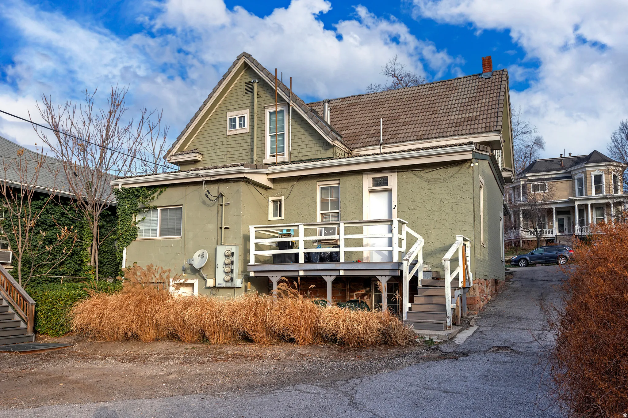 Exterior featuring a pitched tile roof, a second-story deck with white railings, and mature landscaping