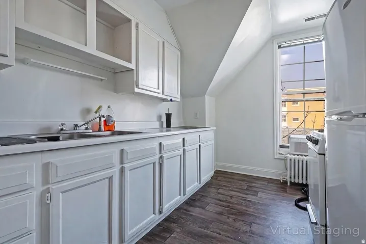 White cabinetry, wood-finish flooring, stainless steel sink, large window, and compact appliances