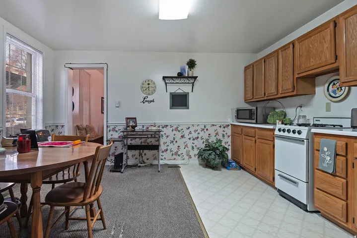 White appliances, wood-finish cabinetry, white countertops, and a window with blinds
