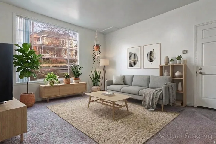 Bright living area with a large multi-pane window, neutral wall finishes, and a paneled entry door
