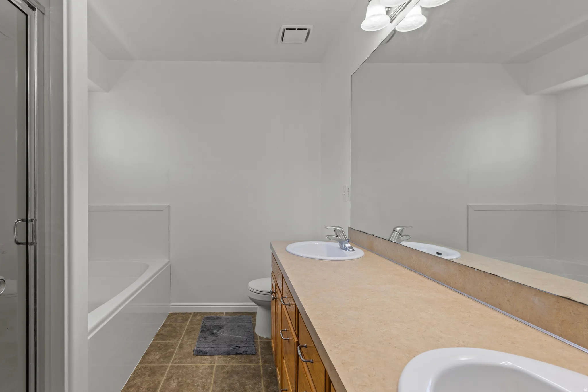 Dual-sink vanity with wood-finish cabinetry, ceramic countertop, and chrome faucetry