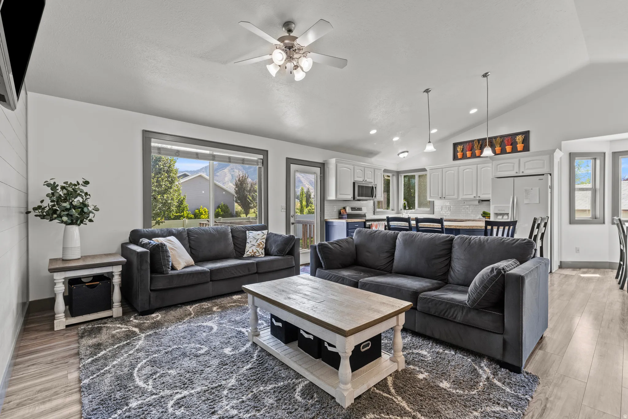 Spacious open-concept living area featuring dual charcoal upholstered sectional sofas, wood-finish flooring throughout, and a wood-top coffee table with storage base