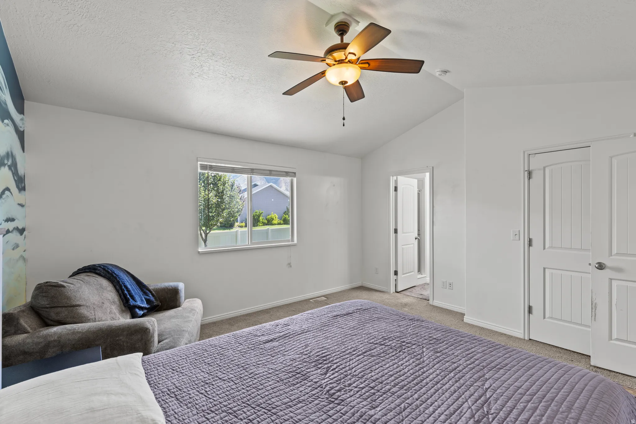 Spacious primary bedroom with ceiling fan, large window with natural light, neutral wall finishes, and direct access to ensuite bathroom and closet space