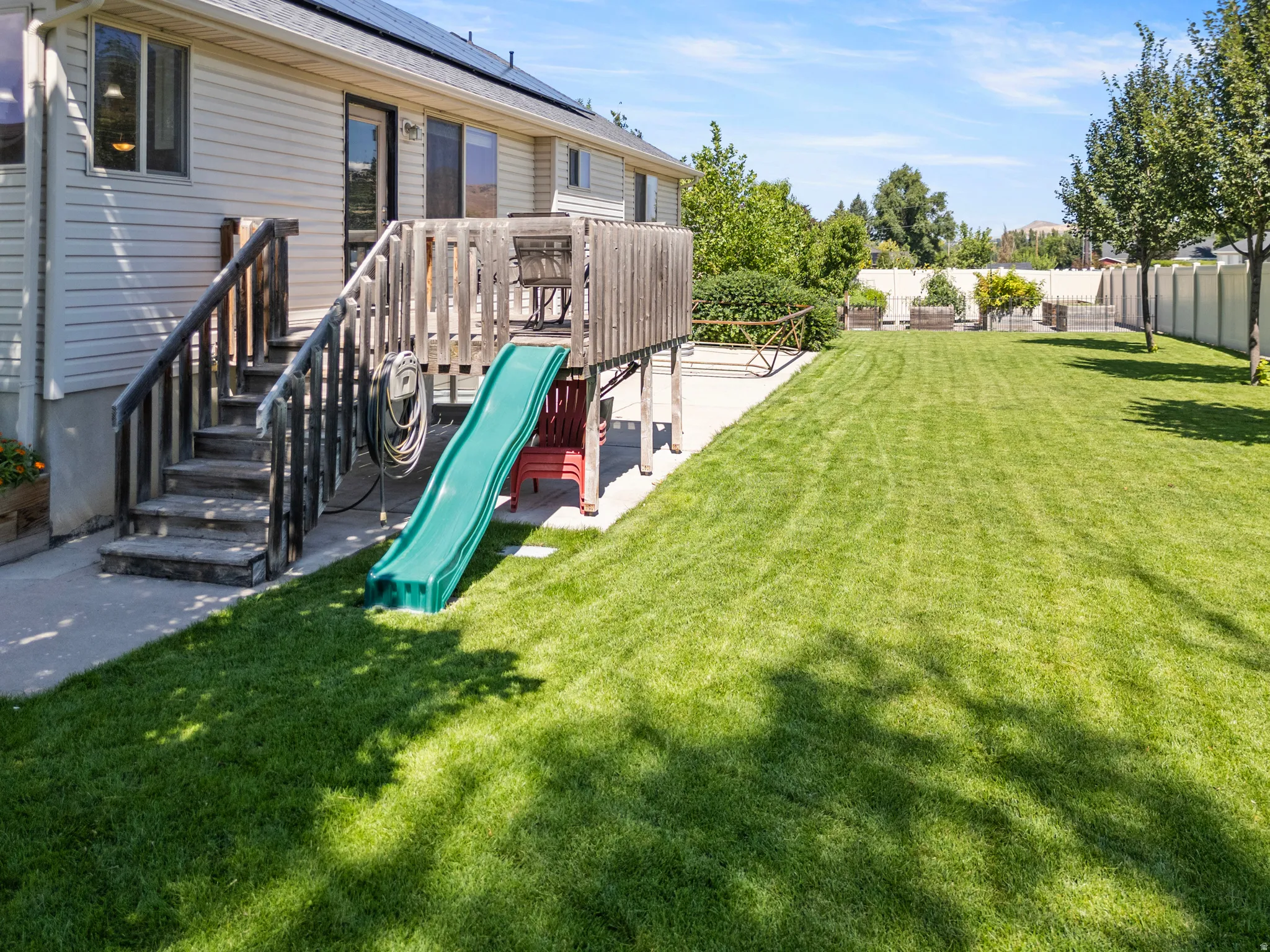 Expansive grassy yard with mature trees, a multi-level wood deck, and solar panels on the roof