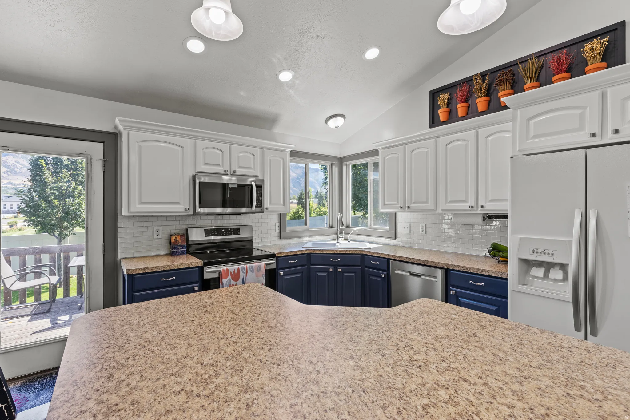 Kitchen featuring white upper cabinetry, blue lower cabinetry, stainless steel appliances, and a light-toned countertop