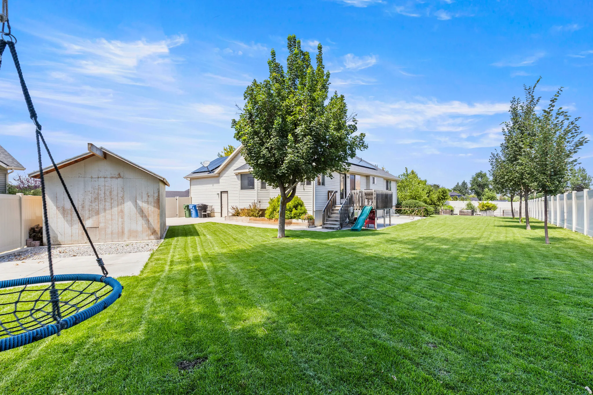 Expansive manicured lawn with mature landscaping, detached garage, trampoline, and mature trees lining the property perimeter