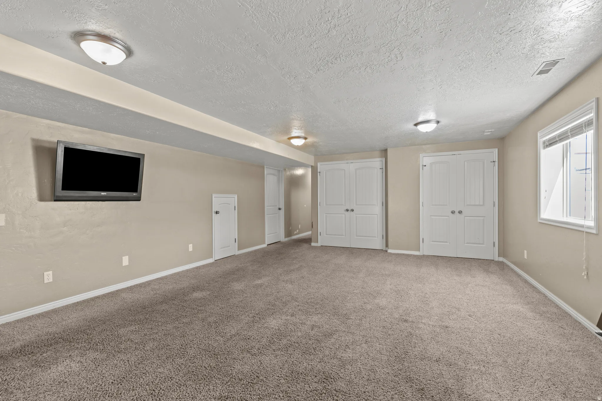 Spacious recreational room featuring neutral carpeting, and multiple closet storage solutions
