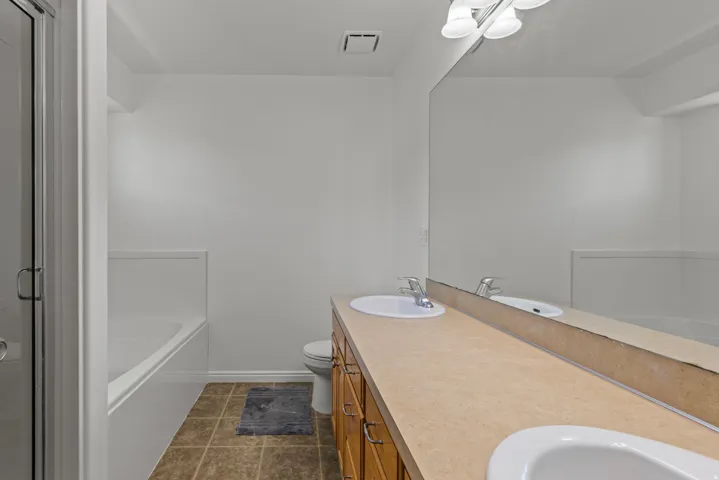 Dual-sink vanity with wood-finish cabinetry, ceramic countertop, and chrome faucetry