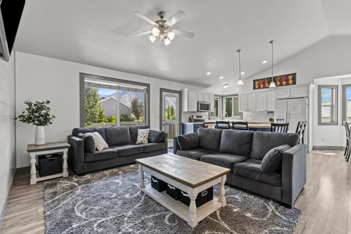 Spacious open-concept living area featuring dual charcoal upholstered sectional sofas, wood-finish flooring throughout, and a wood-top coffee table with storage base