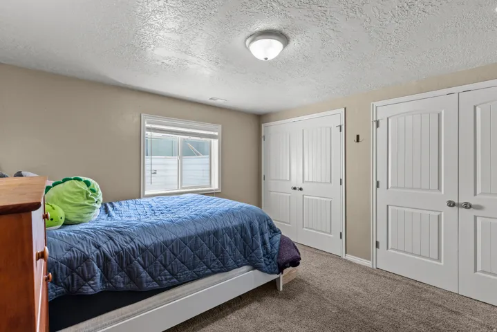 Spacious bedroom featuring carpeted flooring, a large window with blinds, and dual white panel closet doors with interior storage