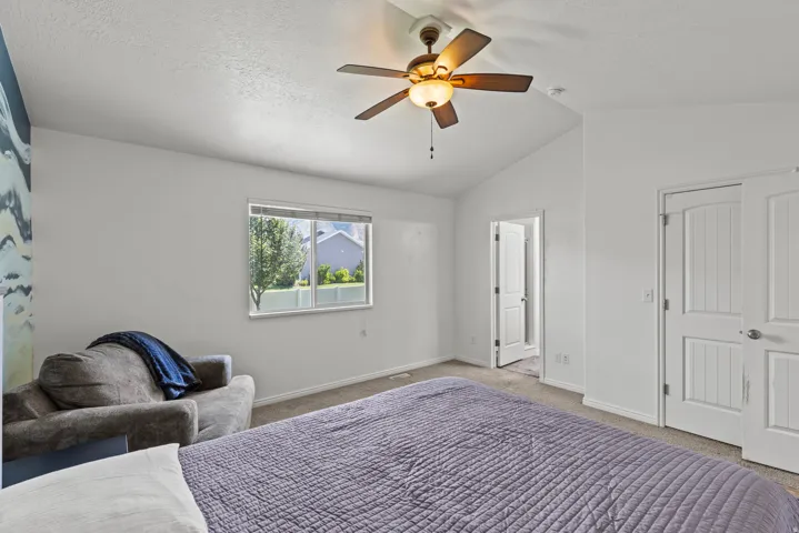 Spacious primary bedroom with ceiling fan, large window with natural light, neutral wall finishes, and direct access to ensuite bathroom and closet space