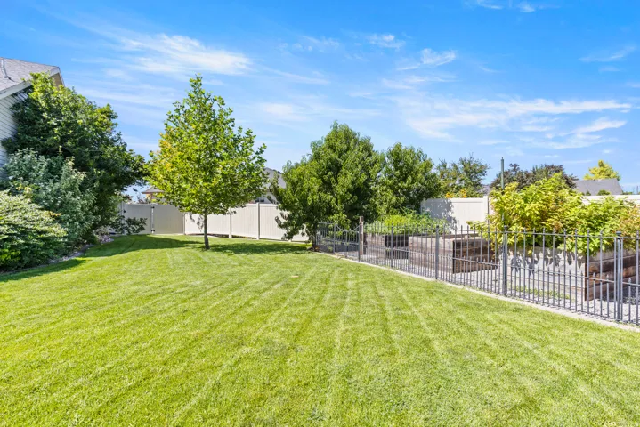Expansive lawn featuring professionally manicured striped turf, mature shade trees throughout the grounds, and decorative metal perimeter fencing